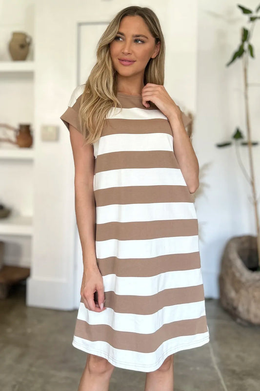 Woman wearing a brown and white striped dress in a room with a white wall and wooden floor.