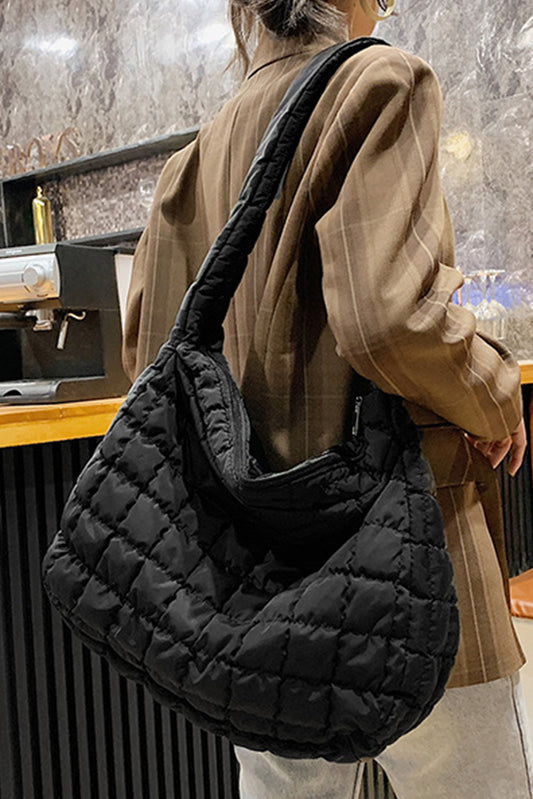 Person holding a black quilted handbag in an indoor setting