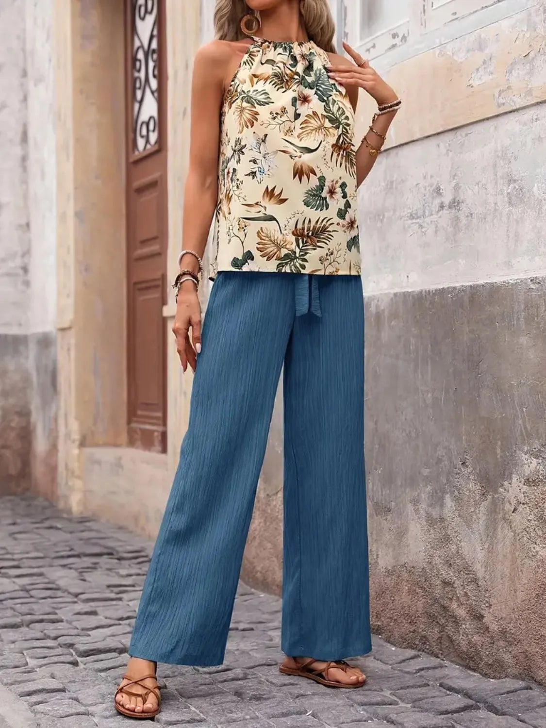 Woman wearing a floral top and blue pants standing on a street.