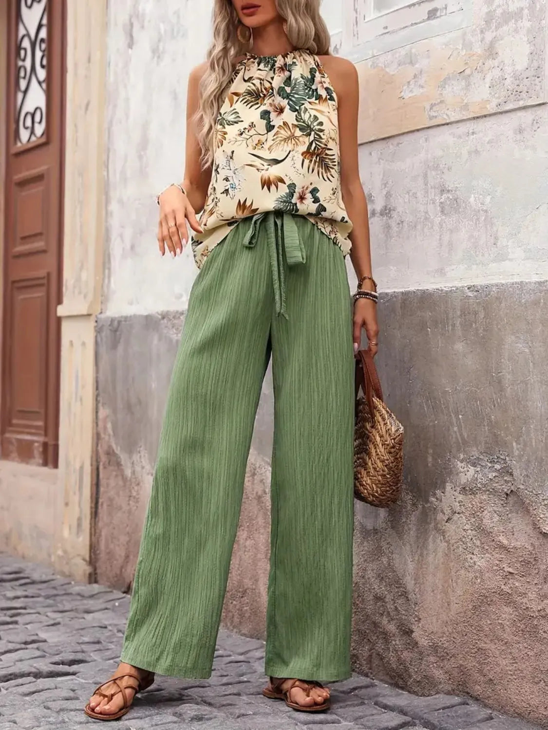 Woman wearing a floral top and green pants standing on a street.