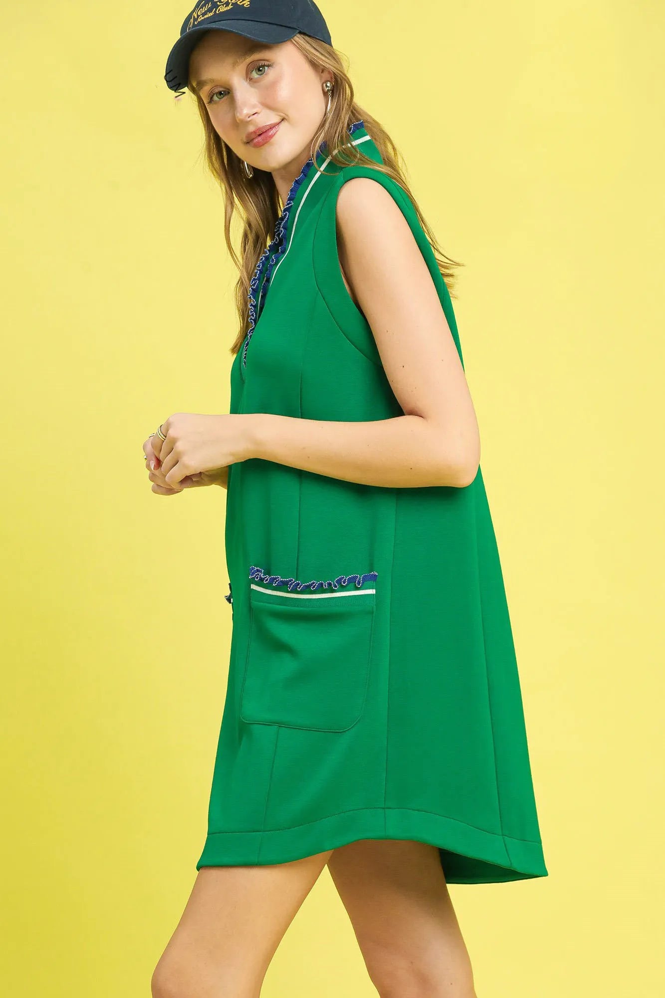 Woman wearing a green dress with blue trim against a yellow background