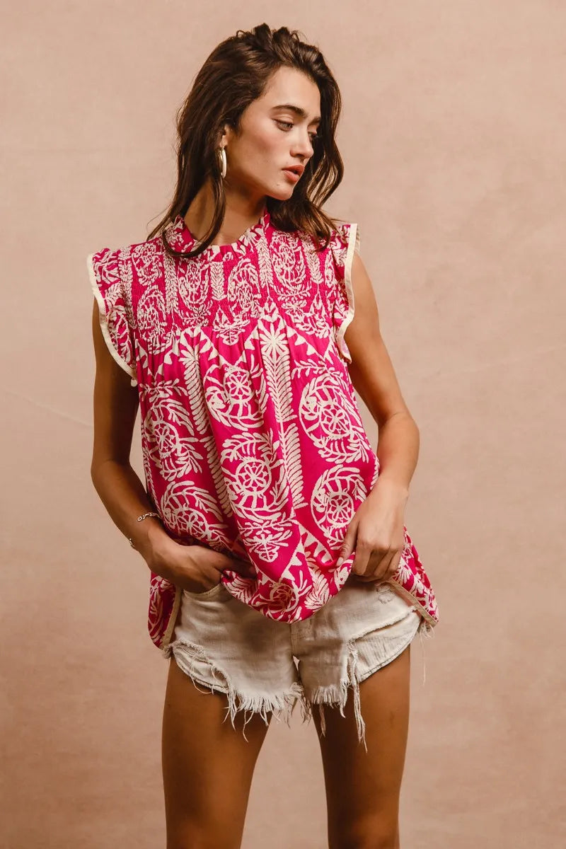 Woman wearing a pink and white patterned top with ruffled sleeves against a beige background