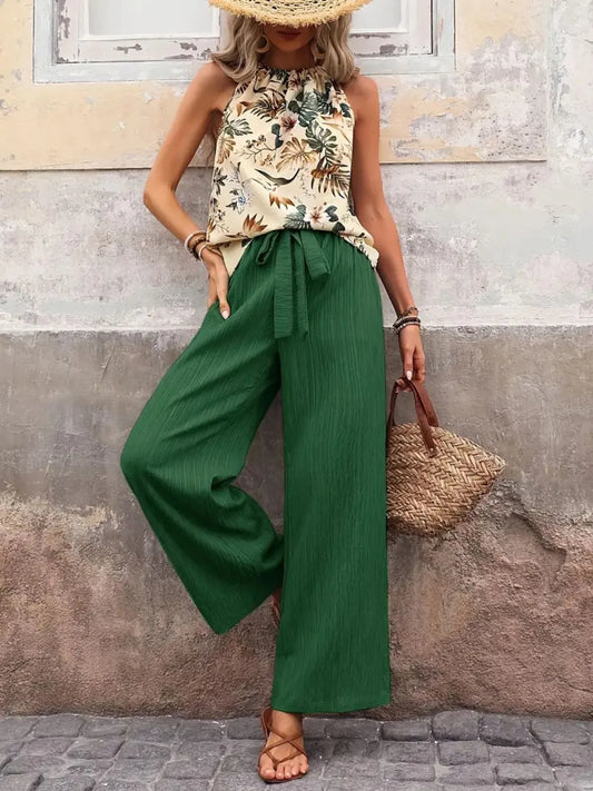 Woman wearing a floral top and green wide-leg pants against a textured wall.