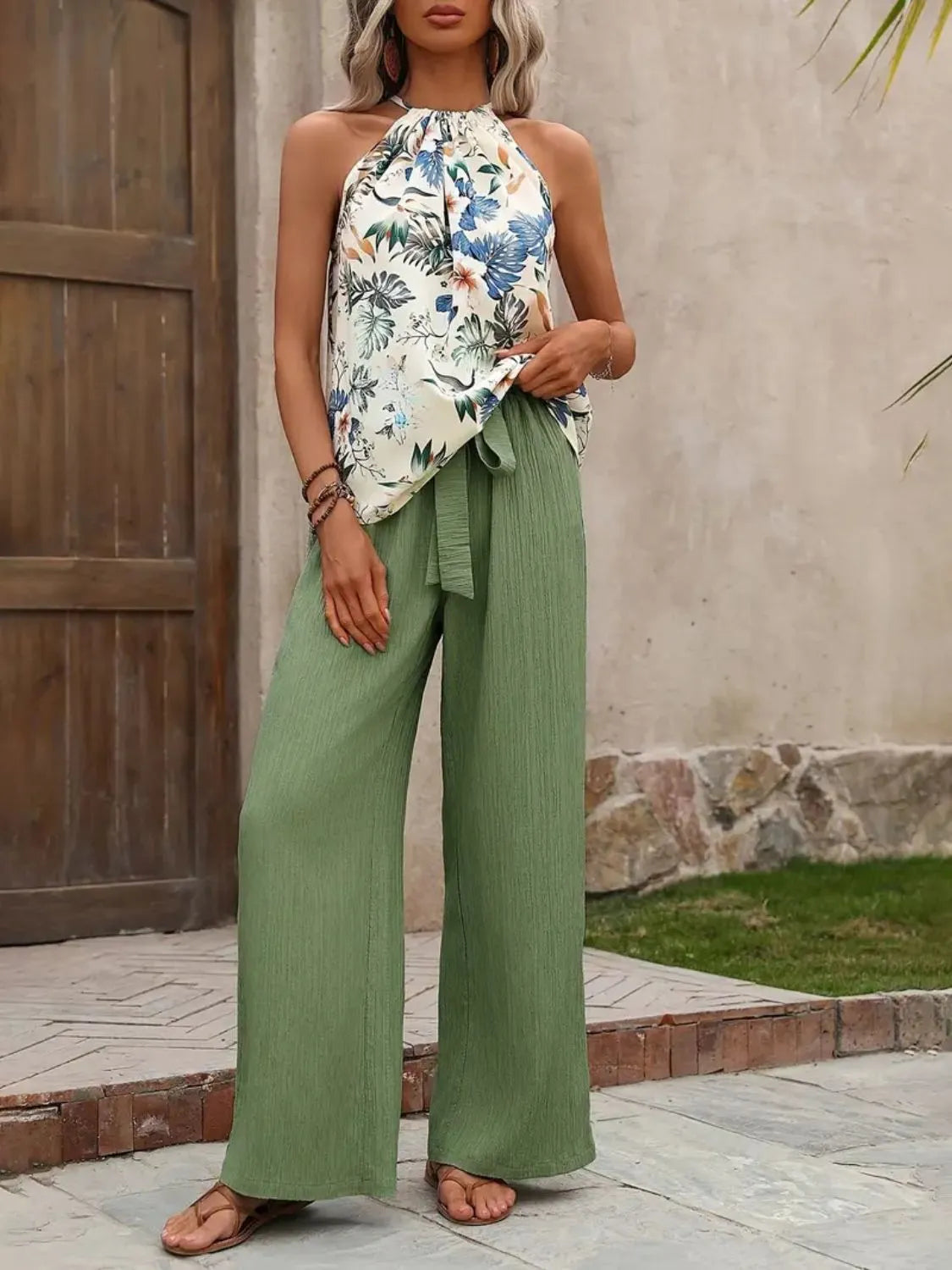 Woman wearing a floral top and green pants standing outdoors.