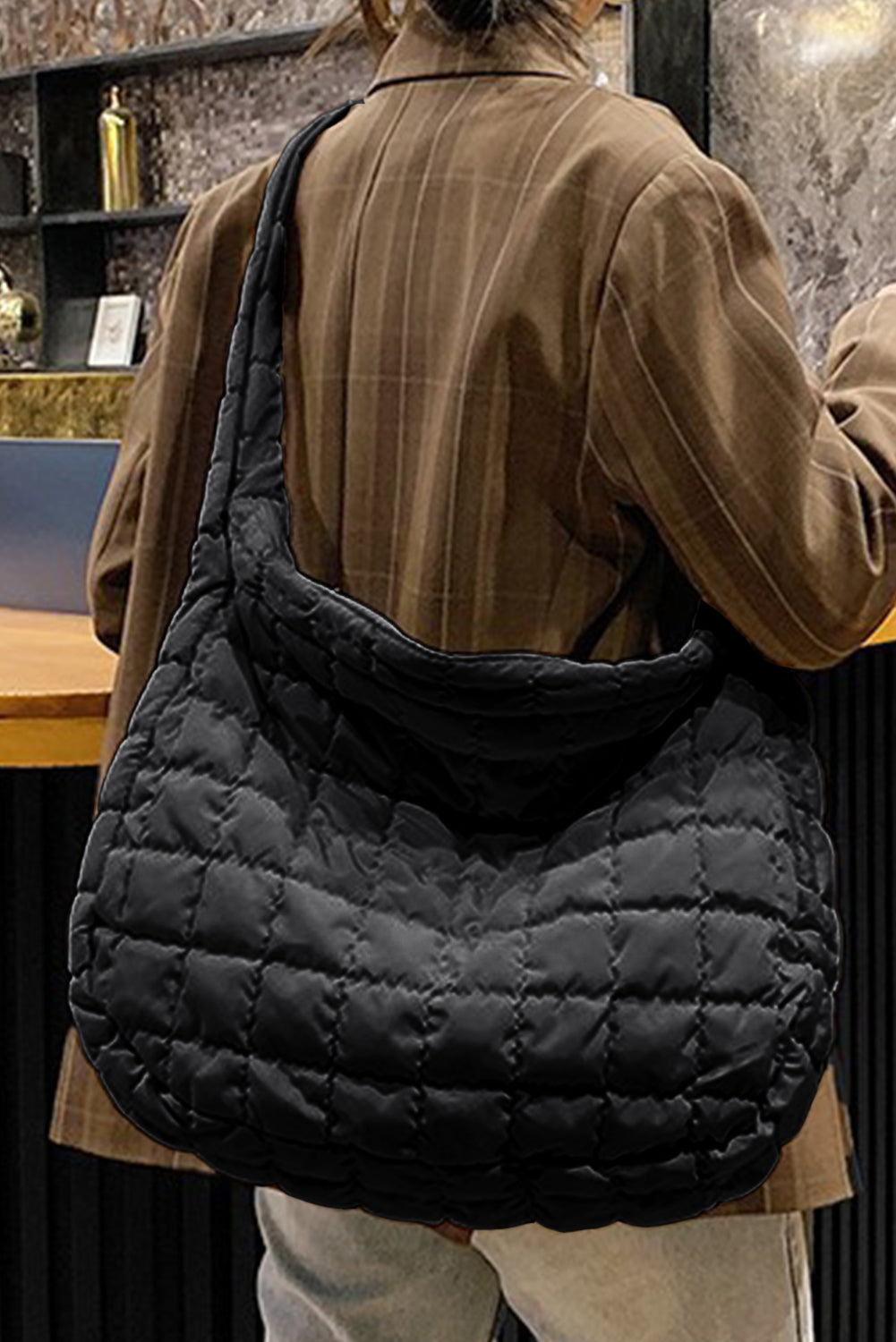 Person wearing a quilted black bag over one shoulder indoors.