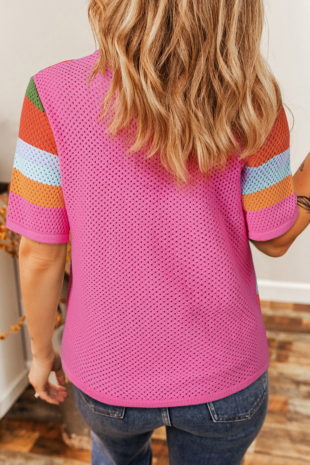 Person wearing a pink mesh top with colorful sleeves indoors