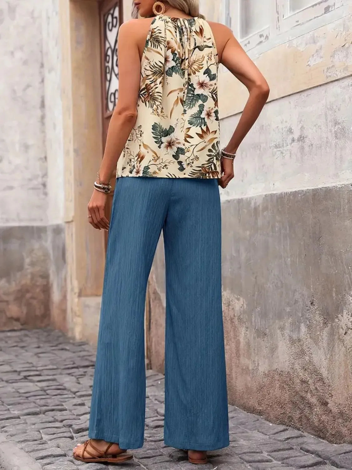 Person wearing a floral sleeveless top and blue wide-leg pants standing on a stone pavement.