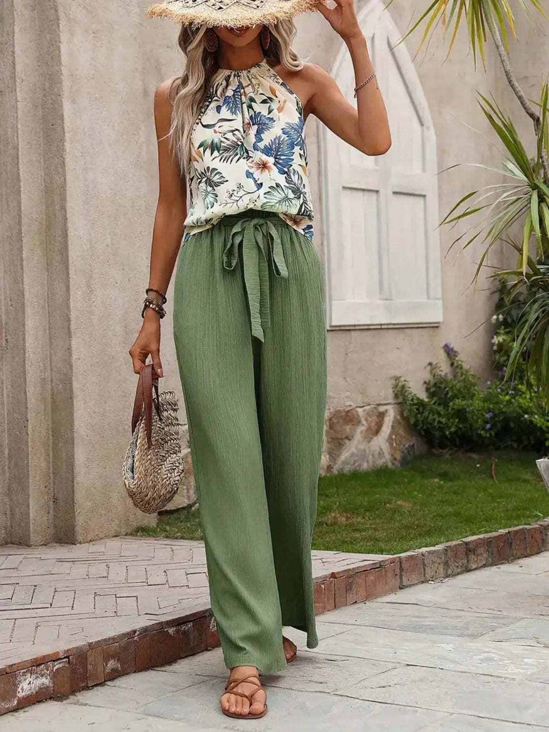 Woman wearing a floral top and green pants standing outdoors.