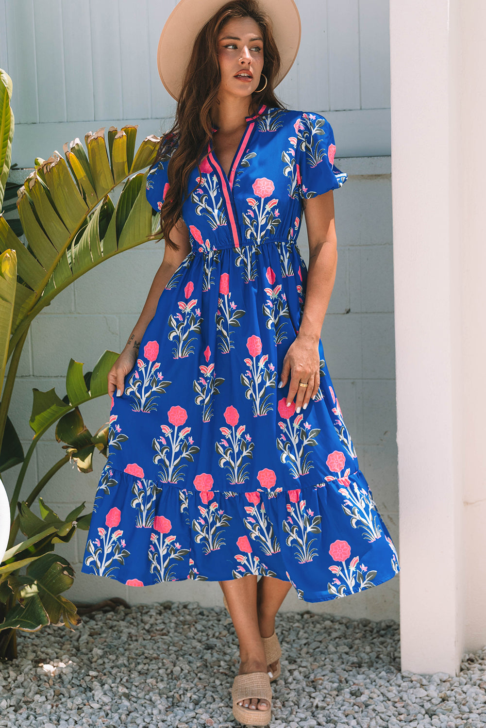 Woman wearing a blue floral dress standing outdoors next to a plant.