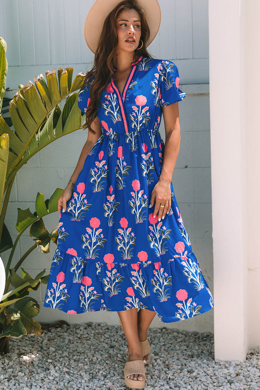 Woman wearing a blue floral dress standing outdoors next to a plant.