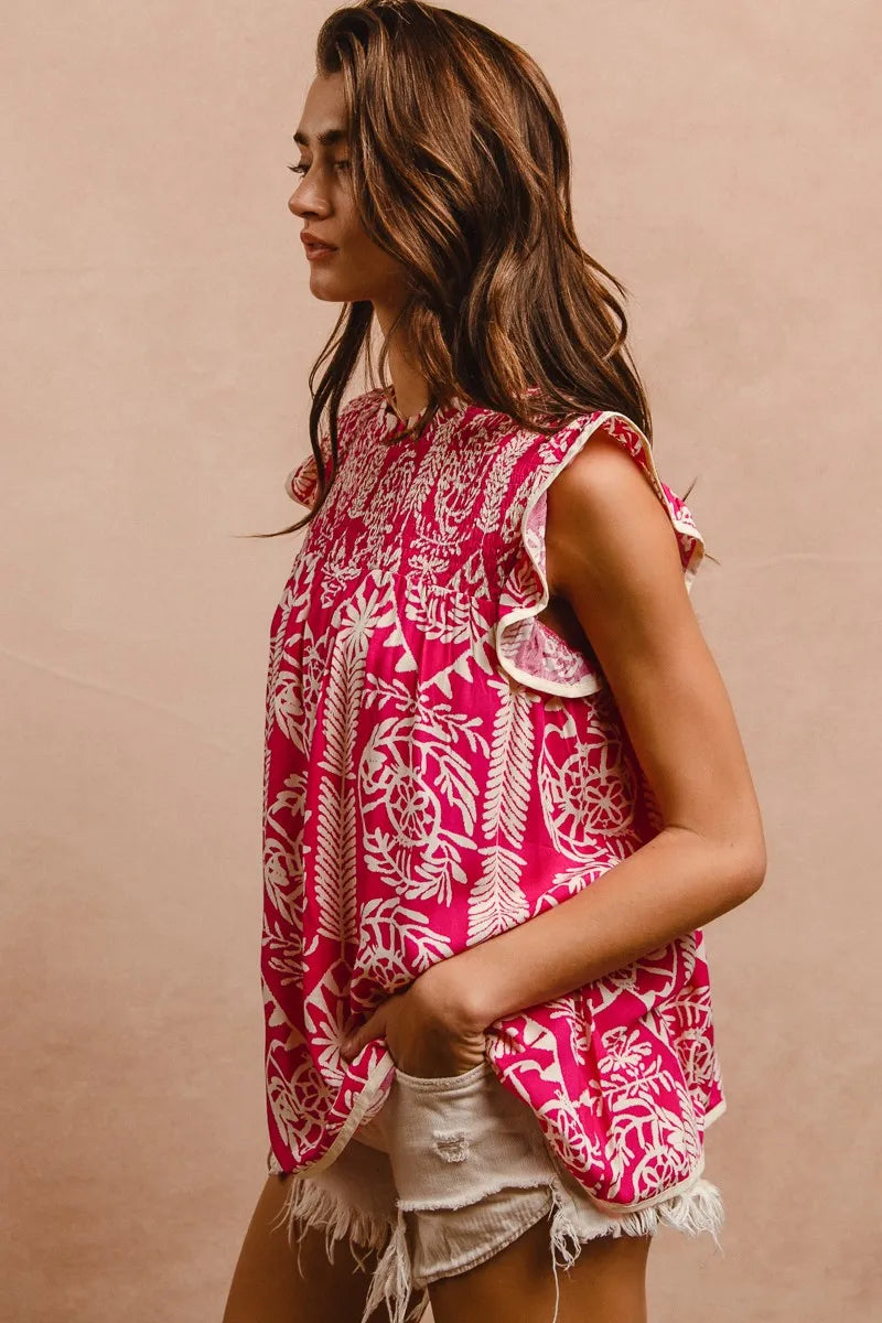 Woman wearing a pink and white patterned top with ruffled sleeves against a beige background
