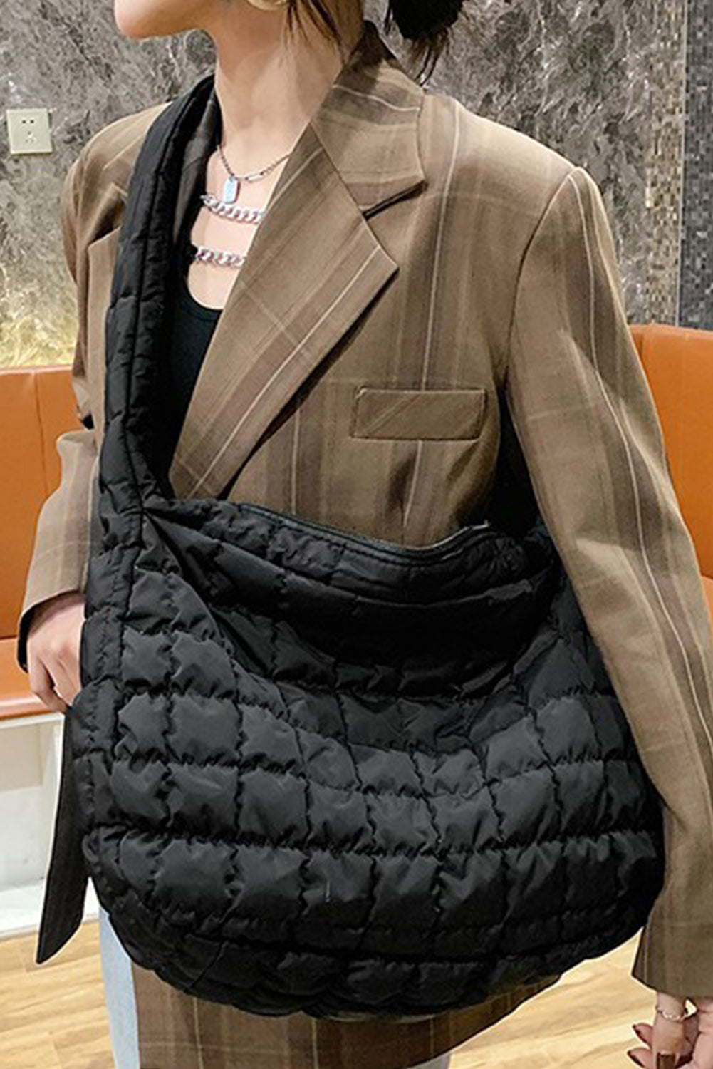 Person wearing a brown blazer and carrying a black quilted bag indoors.