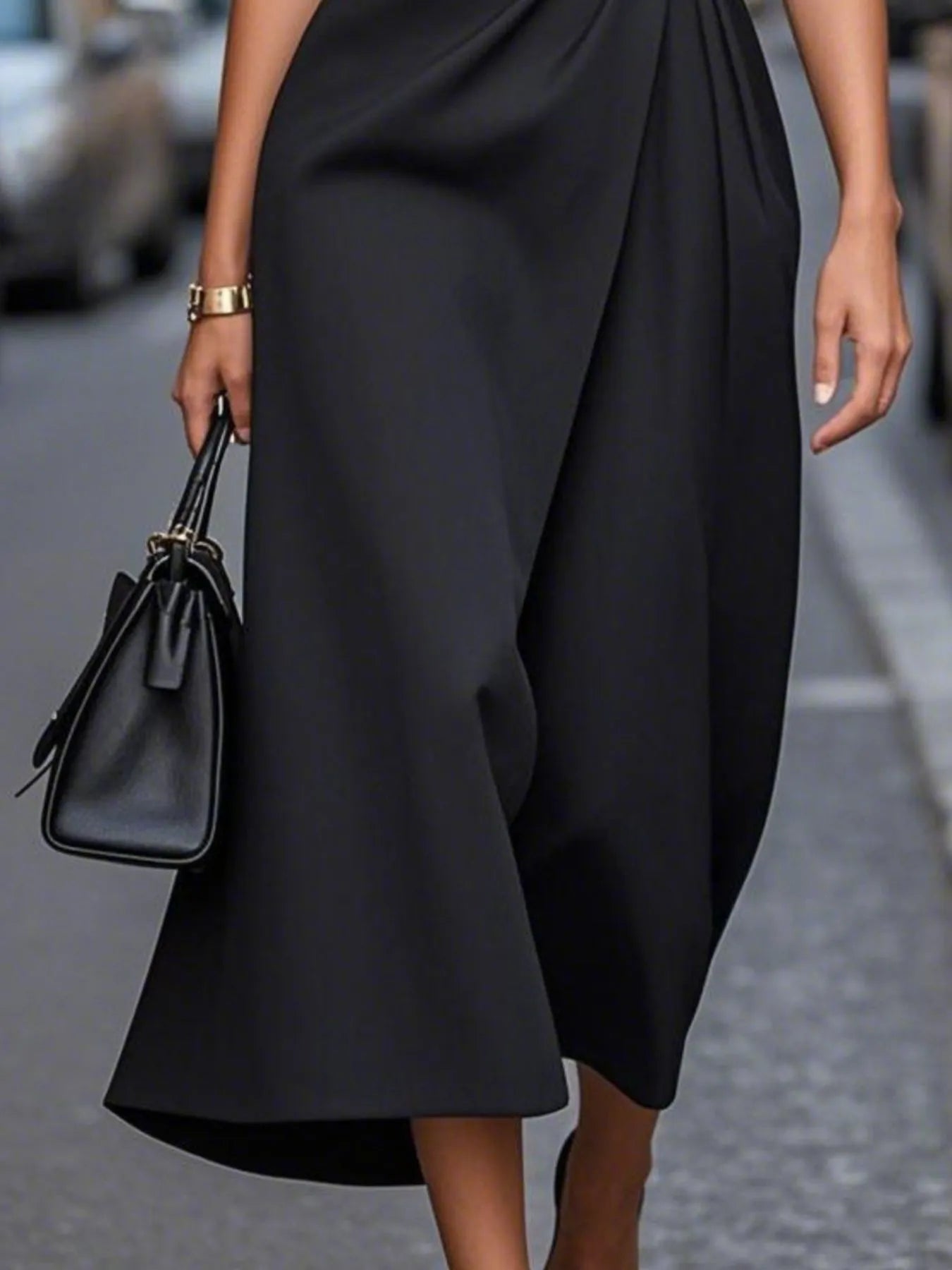 Person wearing a black dress holding a black handbag on a blurred street background