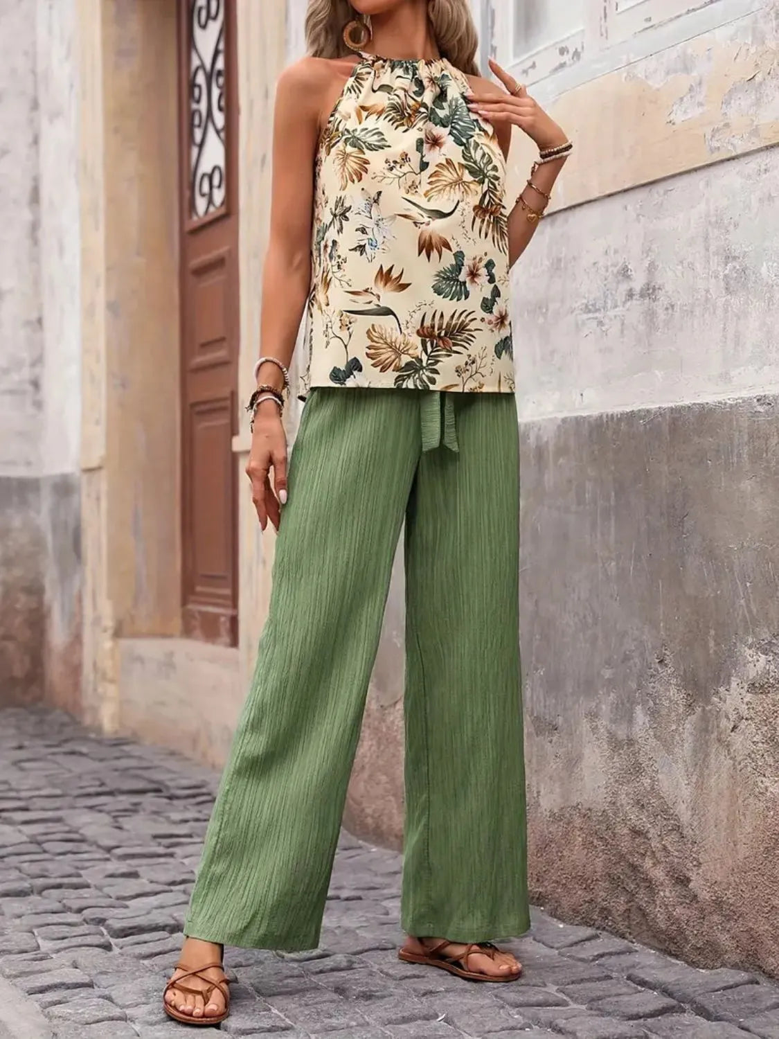 Woman wearing a floral top and green pants standing on a cobblestone street.