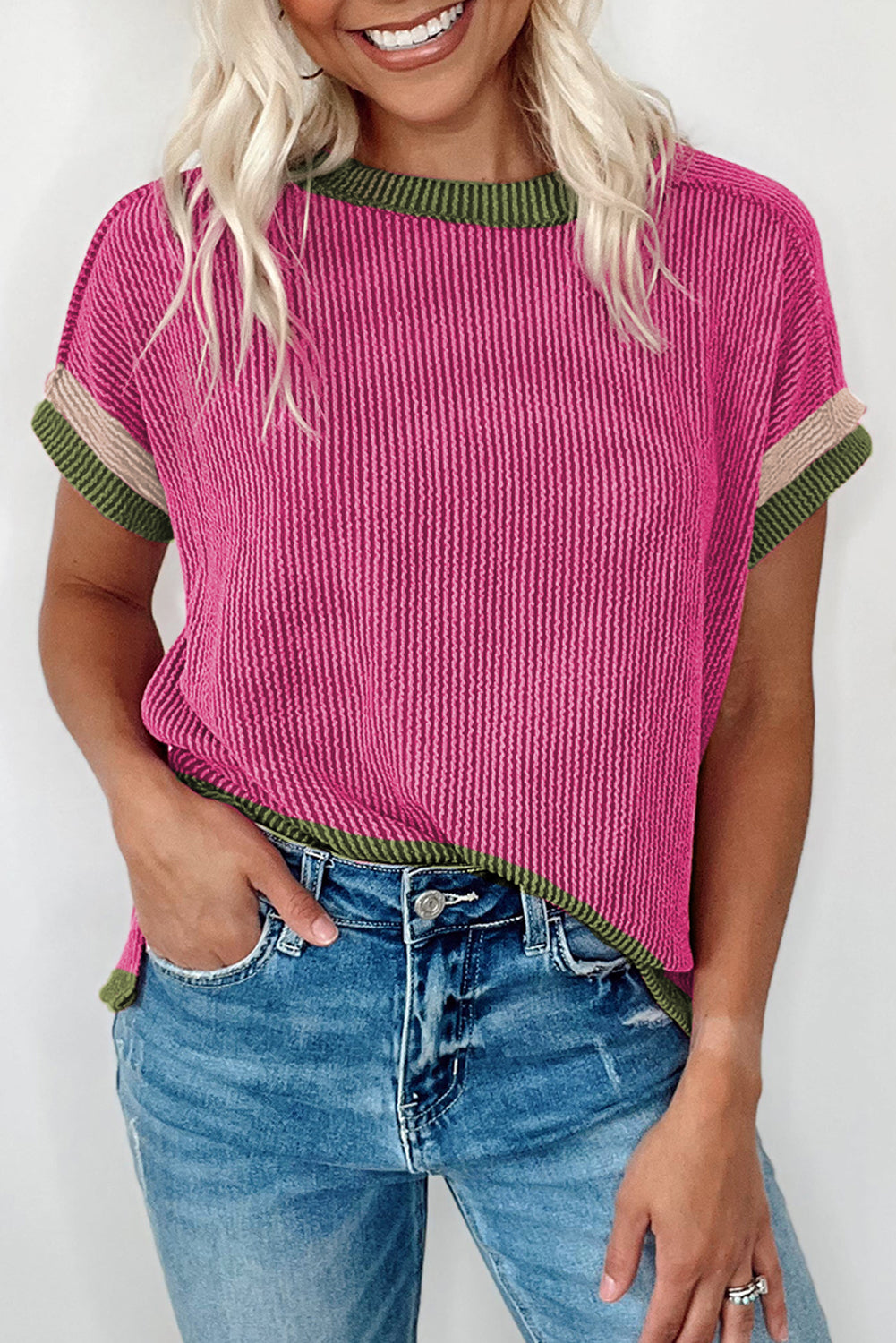 Woman wearing a pink ribbed sweater with green trim and blue jeans against a white background