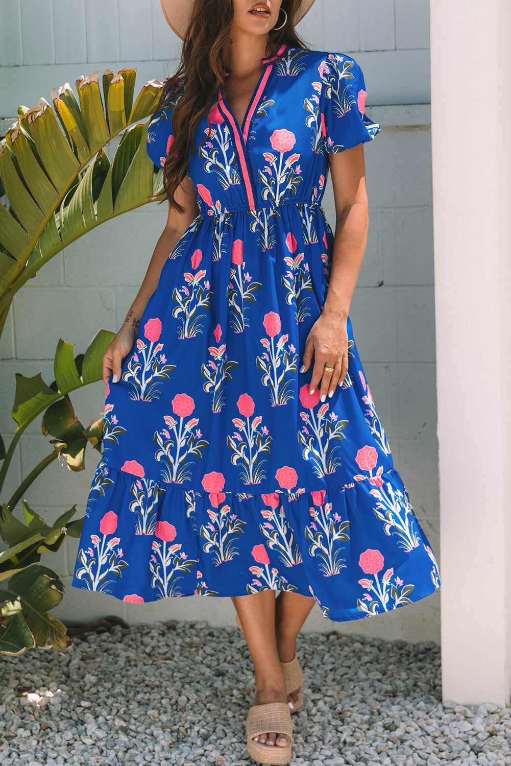 Woman wearing a blue floral dress standing outdoors with greenery in the background