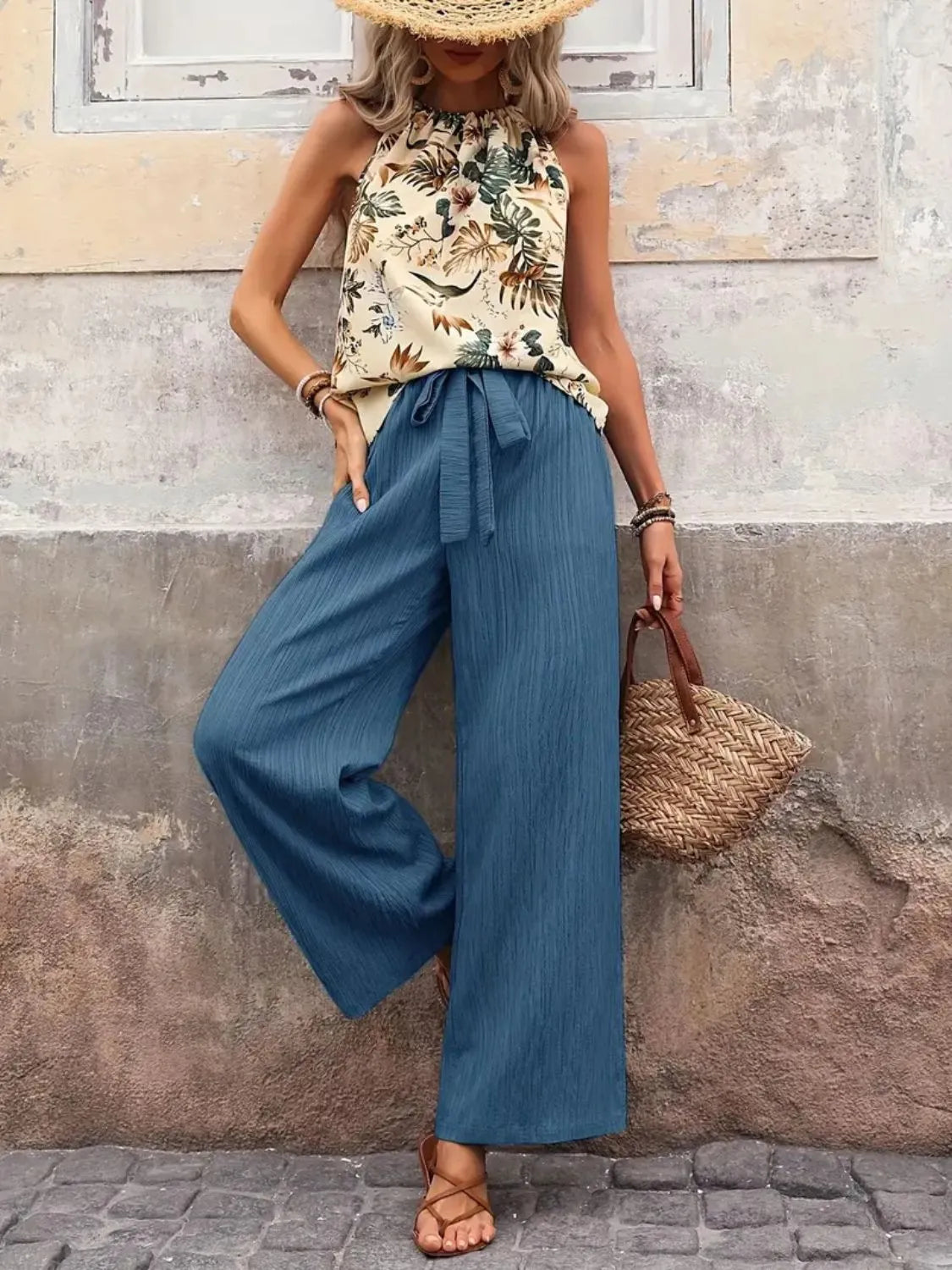 Woman wearing a floral top and blue wide-leg pants against a textured wall.