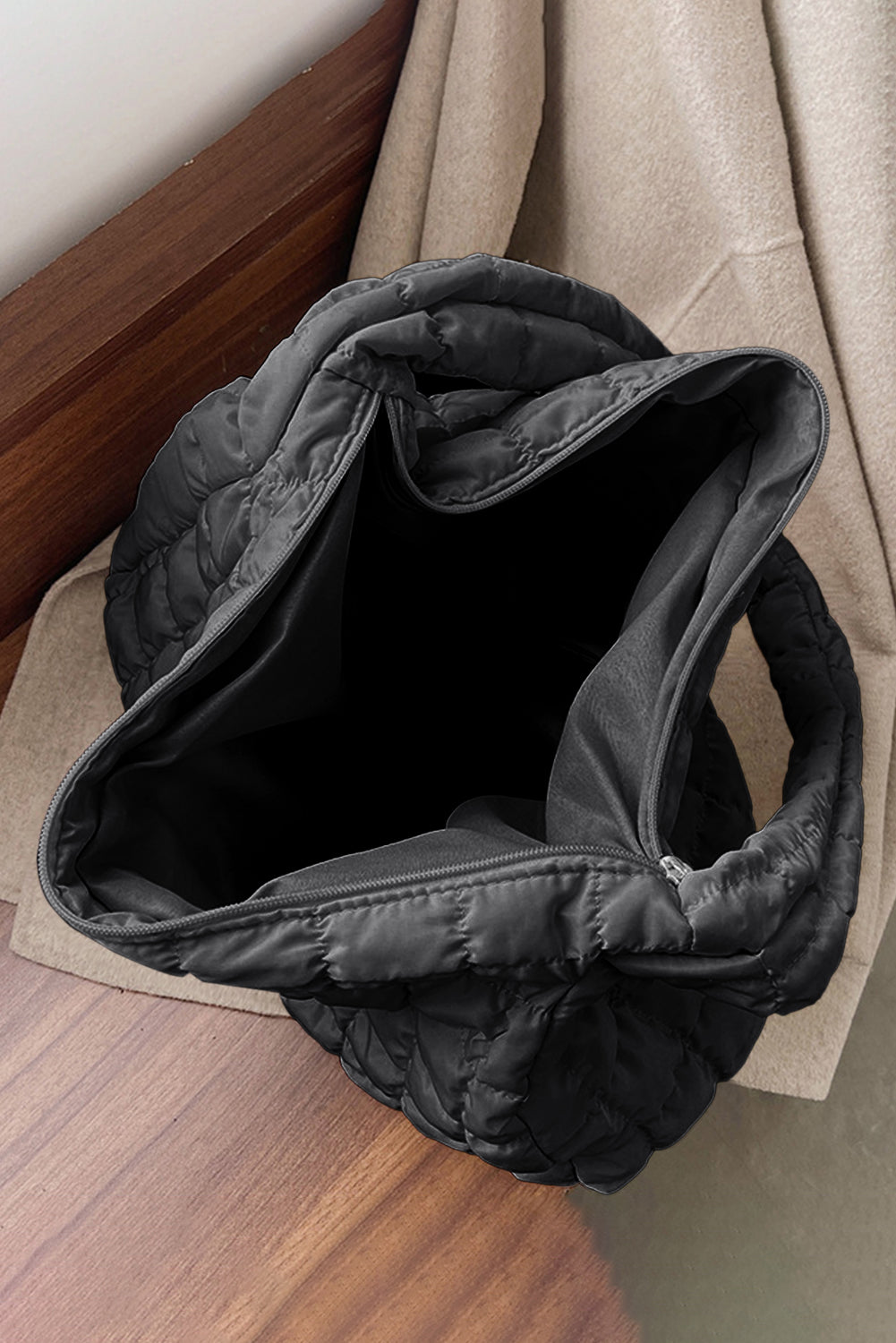 Black quilted jacket on a wooden surface with a beige coat in the background
