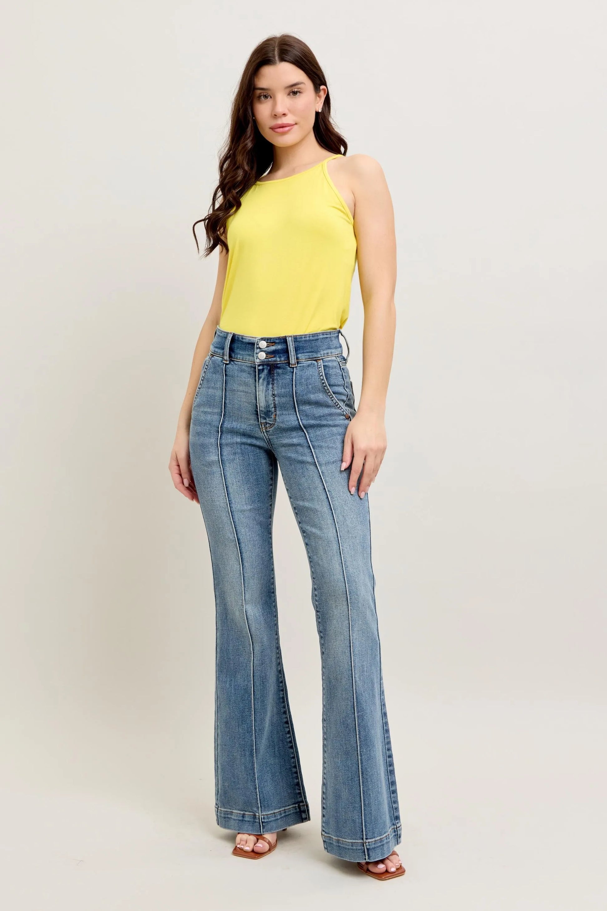Woman wearing a yellow top and blue flared jeans on a white background