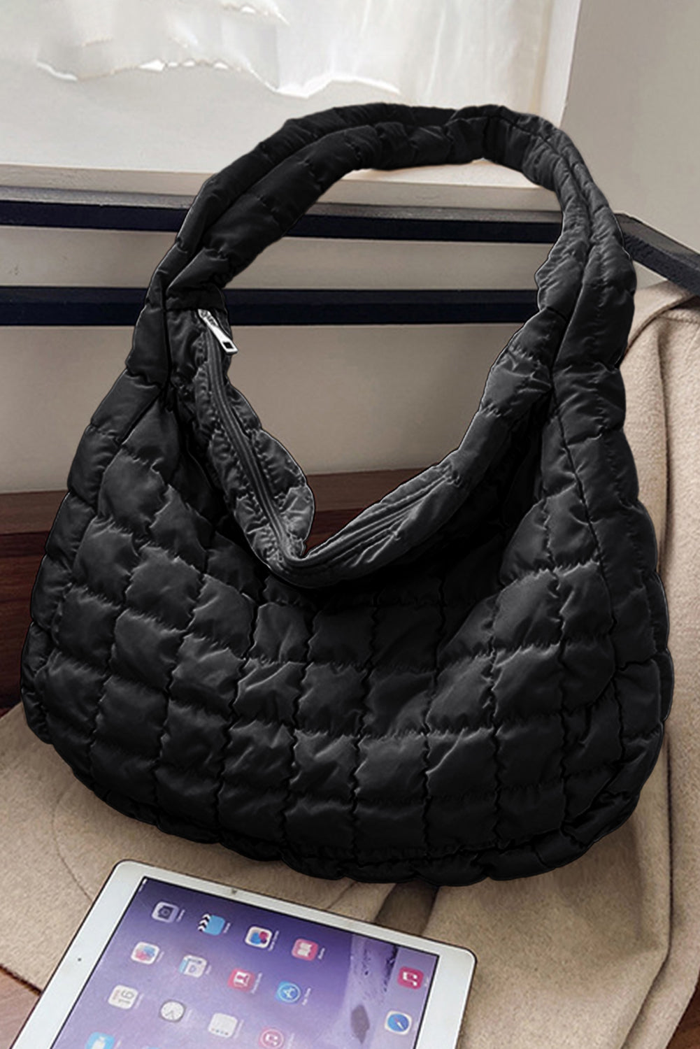 Black quilted handbag on a beige surface with a tablet in the foreground