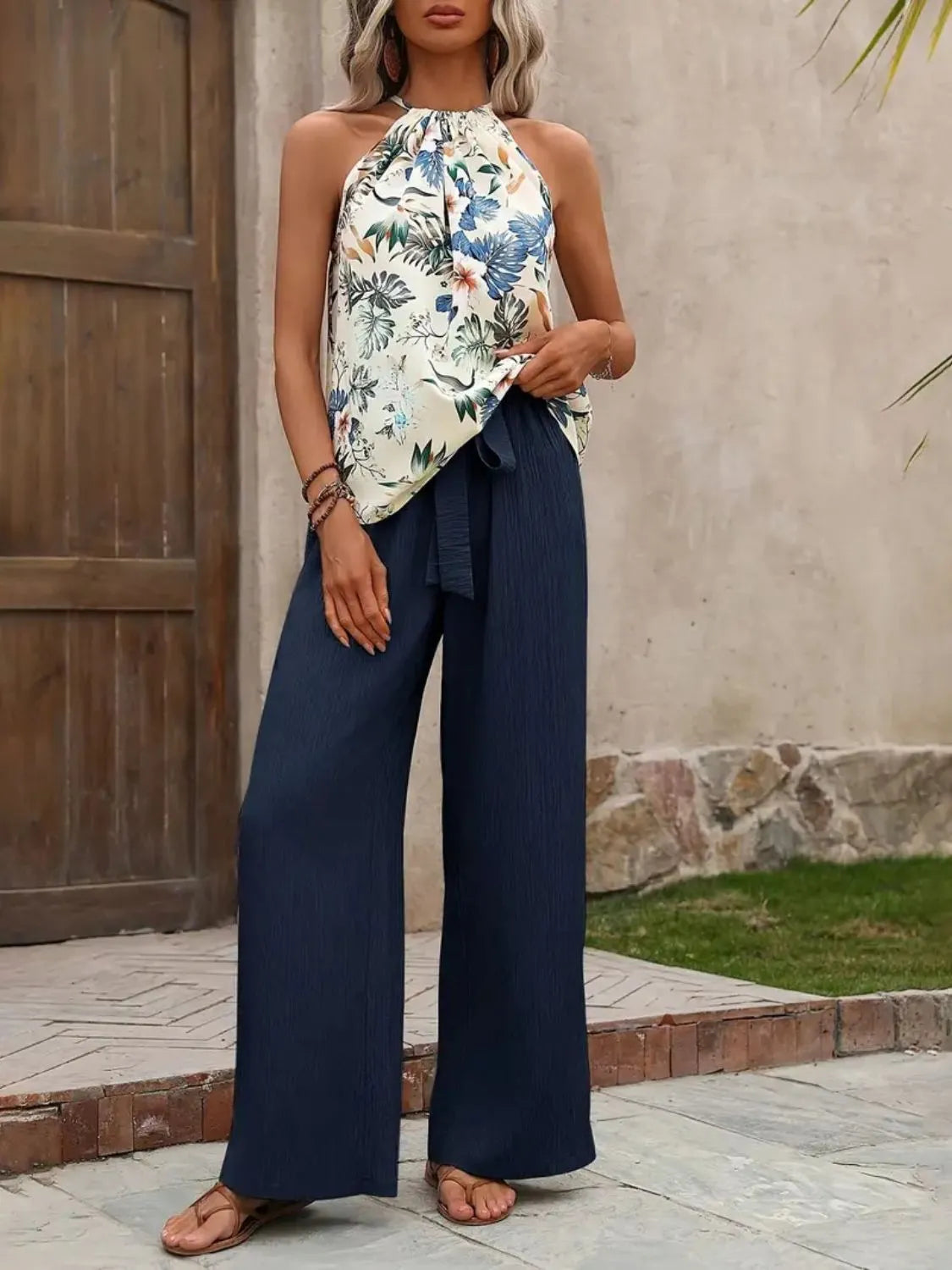 Woman wearing a floral top and navy pants standing outdoors.