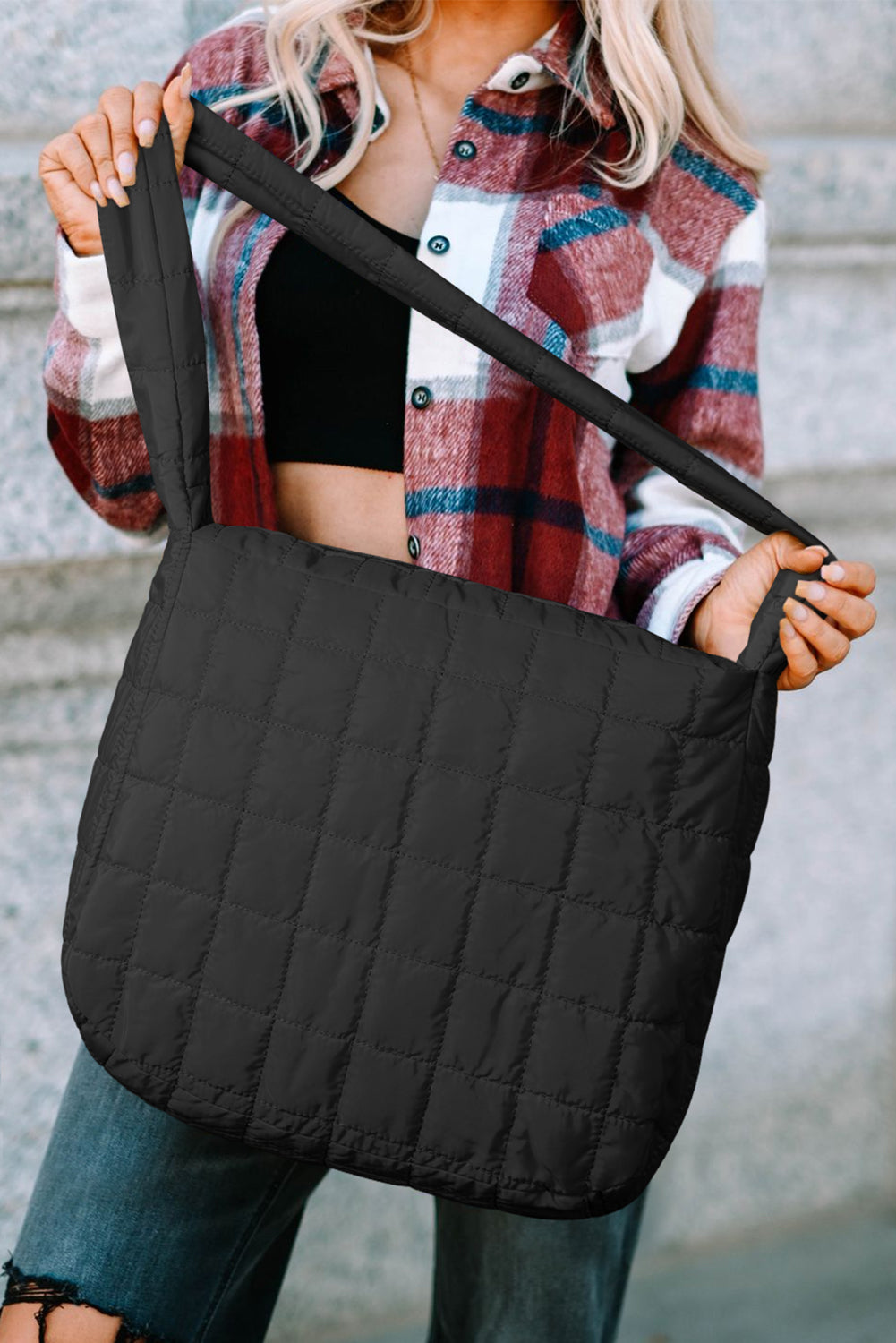 Person holding a black quilted bag with a blurred background